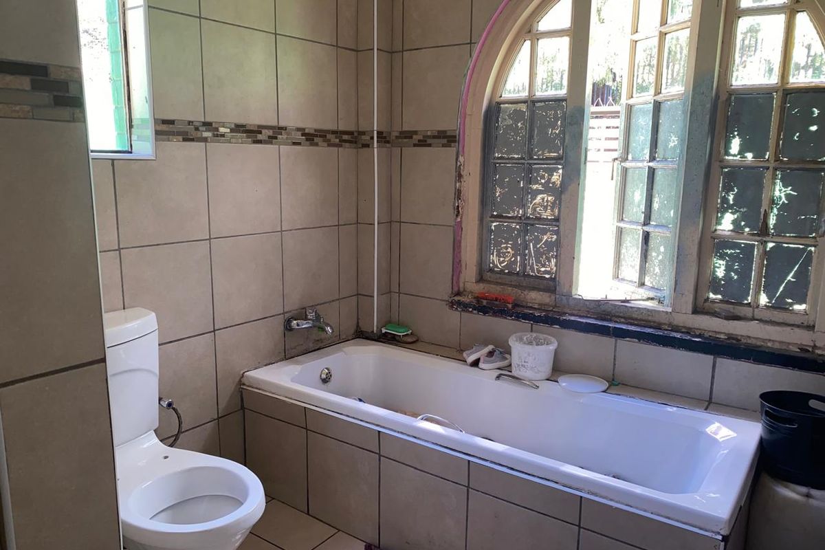 A bathroom featuring a built-in bathtub with tiled surround, a standard toilet, and an arched window with visible wear on the frames.