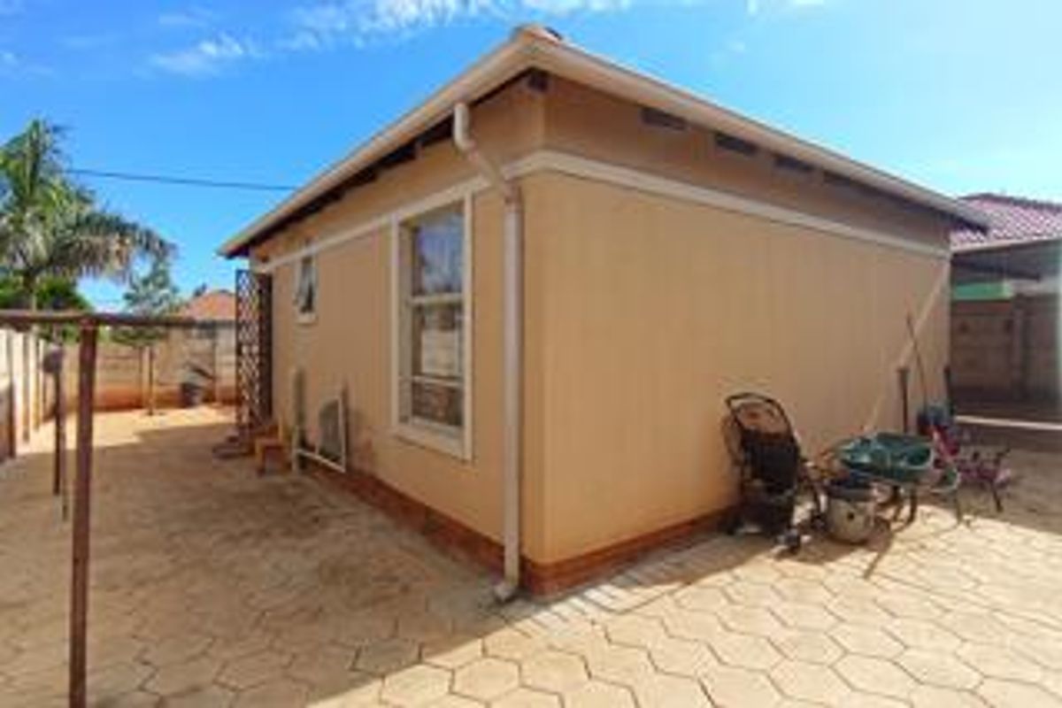 A view of the rear exterior of the house featuring paved ground surfaces and a simple building facade.