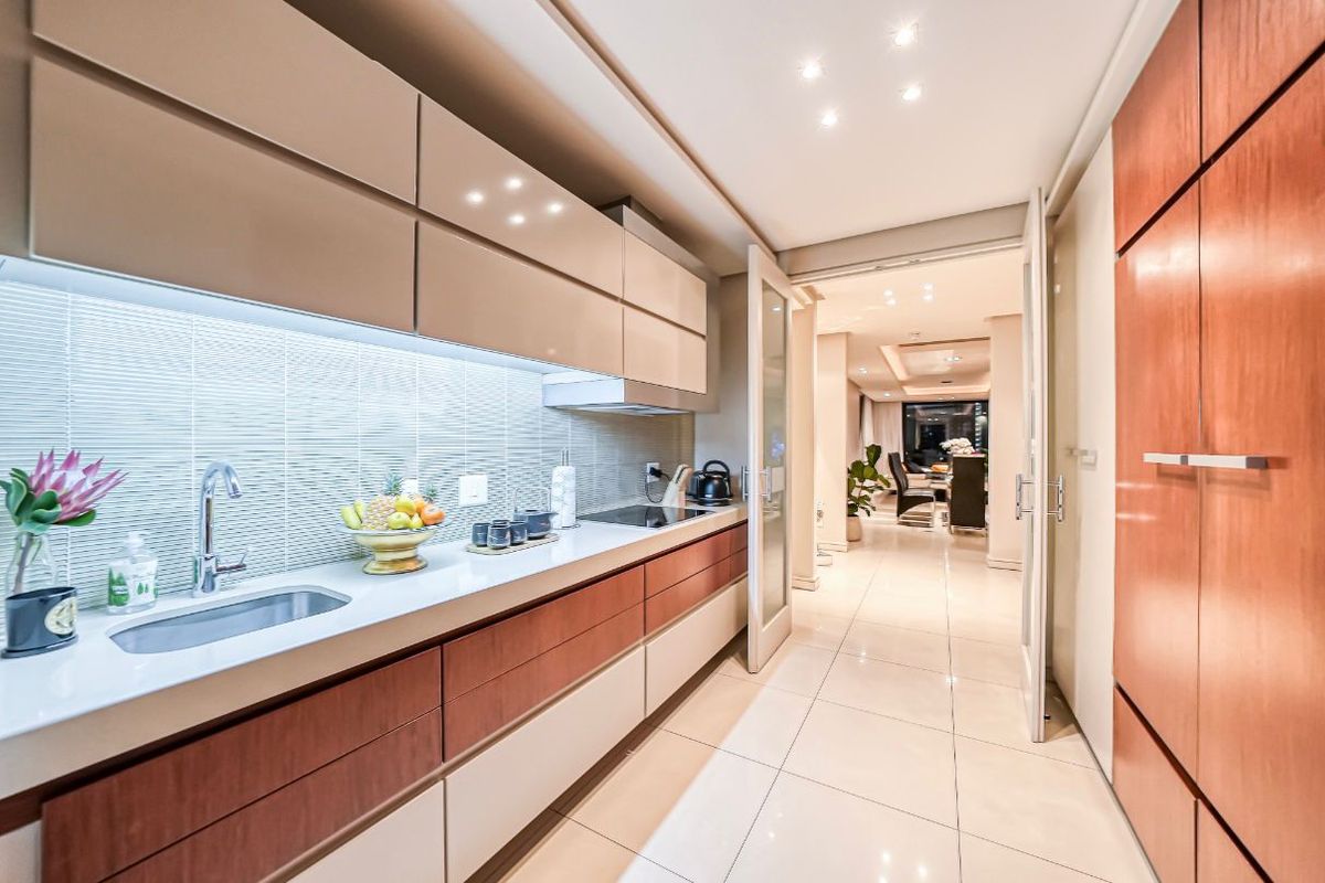 Modern galley-style kitchen featuring sleek cabinetry, integrated cooktop, under-cabinet lighting, and high-quality tiled flooring, leading into an open-plan living area.