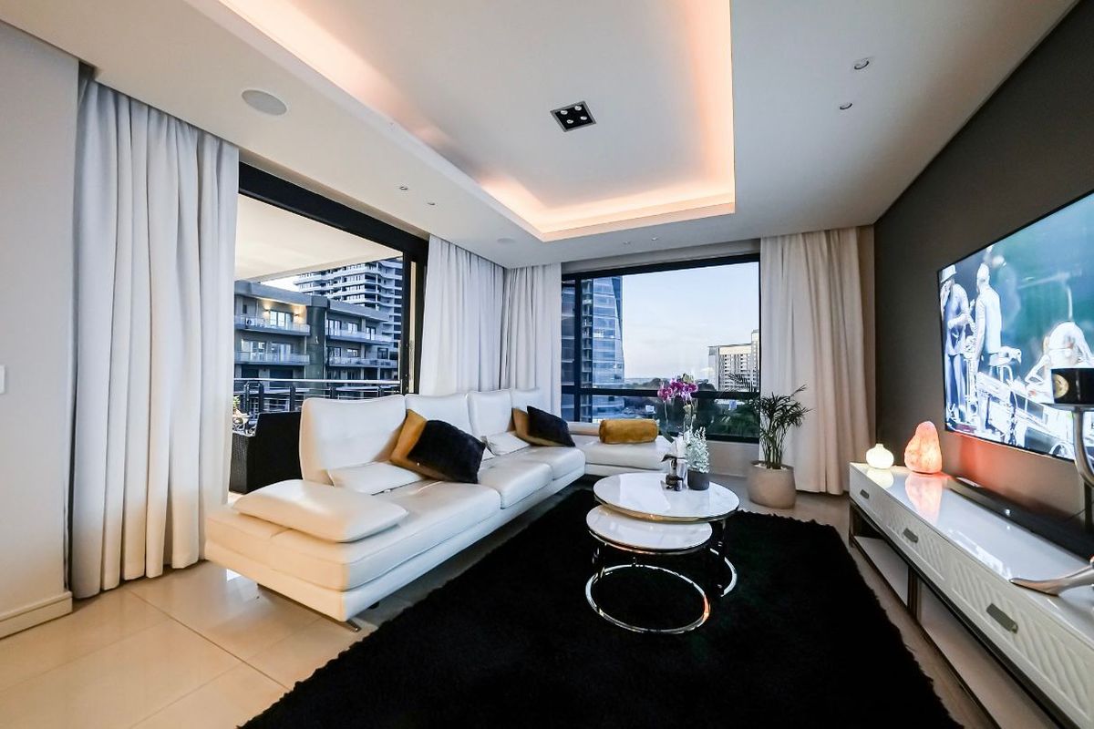 Modern living room featuring recessed ceiling lighting, large windows with city views, and seamless access to an outdoor balcony area.