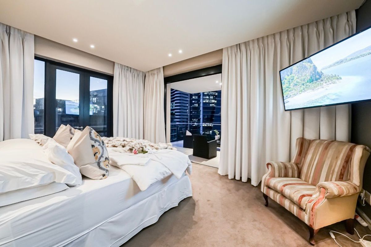 Modern bedroom featuring recessed ceiling lighting, floor-to-ceiling curtains, and direct access to a private balcony with city views.