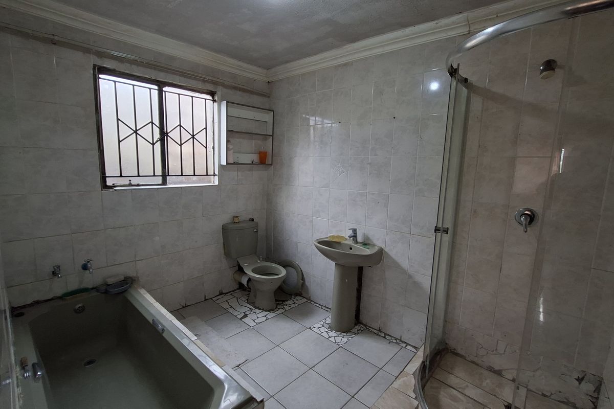 A dated bathroom featuring a bathtub, pedestal basin, toilet, and a separate shower enclosure with tiled walls and flooring.