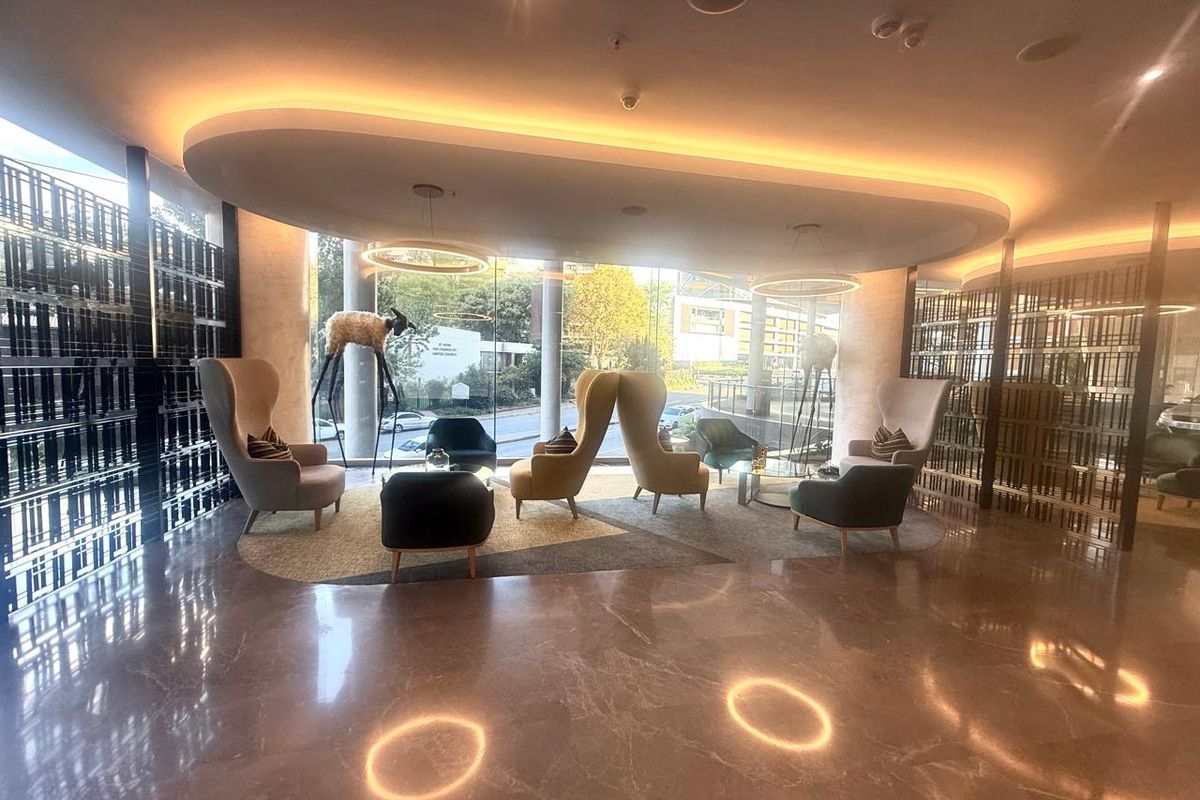 Modern lobby or lounge area featuring polished marble flooring, recessed cove lighting, and decorative metal room dividers in a contemporary apartment building.