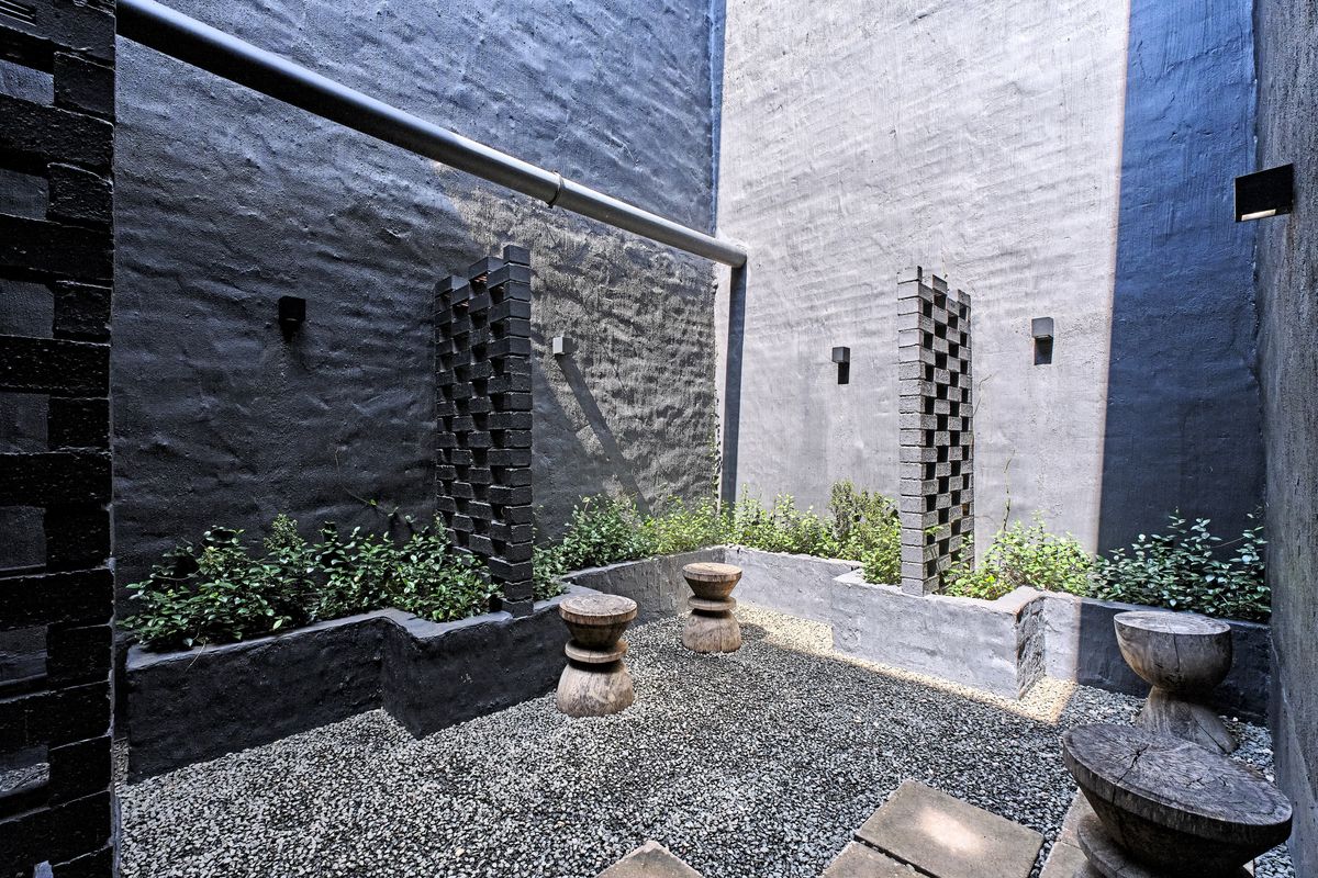 A private courtyard featuring gravel flooring, built-in brick planters, and decorative brick privacy screens against high painted masonry walls.