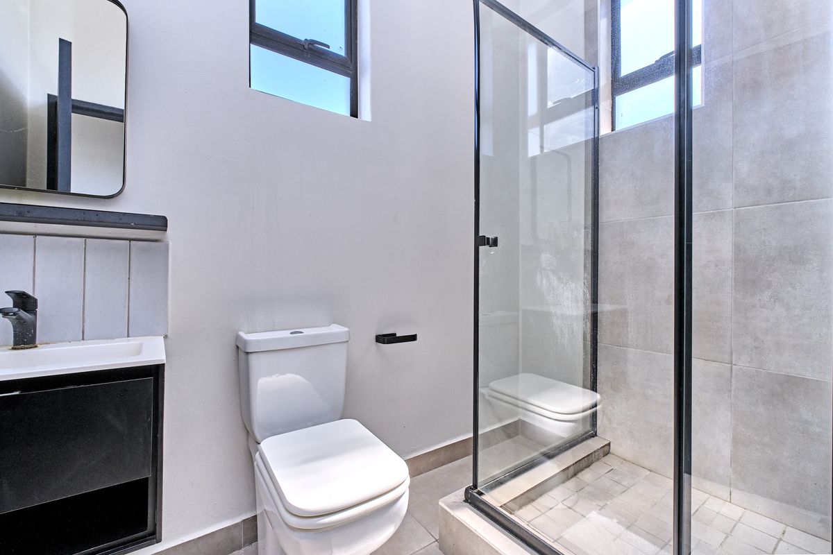 Modern bathroom featuring a glass-enclosed shower, contemporary vanity with black fixtures, and neutral floor-to-ceiling tiling.