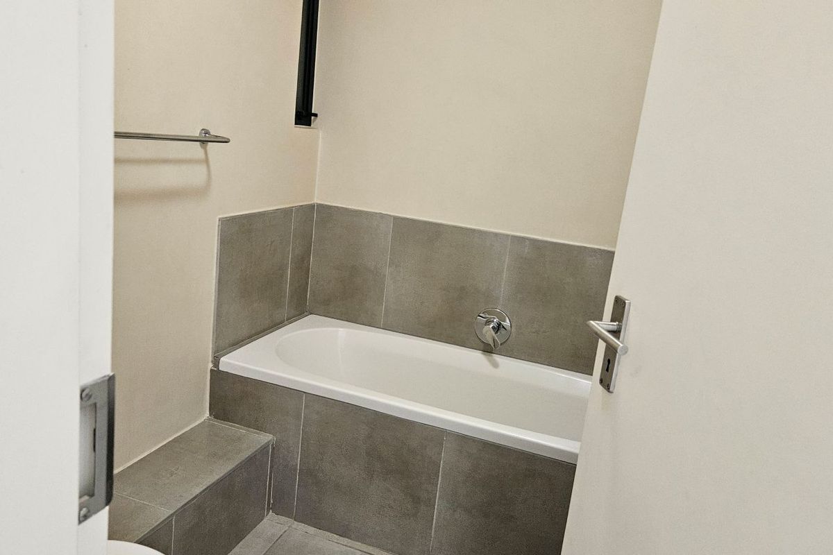 A clean bathroom featuring a built-in bathtub with grey tiled surround and a wall-mounted towel rail.