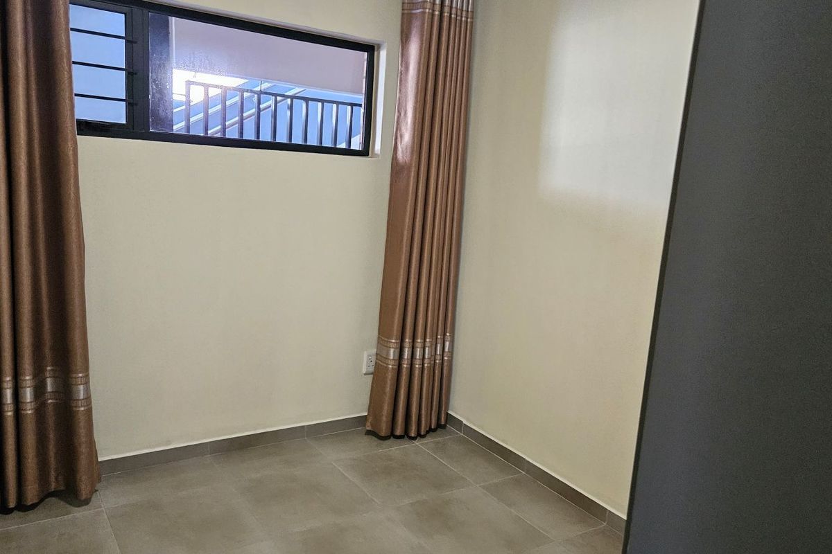 A clean, neutral bedroom featuring tiled flooring, a horizontal window with security bars, and installed curtain tracks.