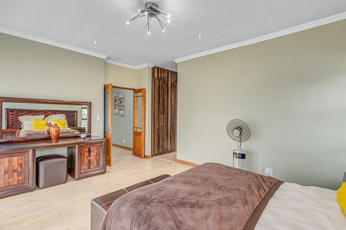 Spacious bedroom featuring light wood-look flooring, built-in floor-to-ceiling wooden cupboards, decorative crown molding, and a modern starburst ceiling light fixture.