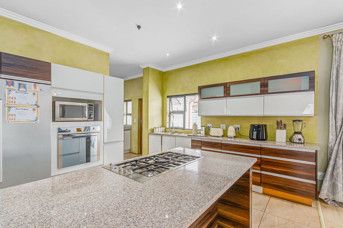 Modern kitchen featuring a central island with a built-in gas hob, granite countertops, and two-tone cabinetry with integrated oven and microwave.