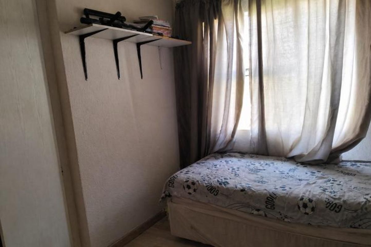A compact bedroom featuring laminate flooring, a built-in wall shelf, and a window dressed with curtains.