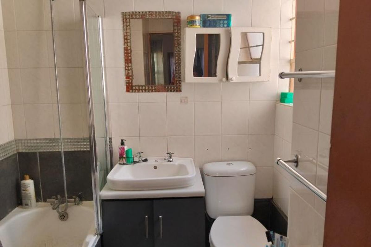 A functional bathroom featuring a shower-over-bath combination, a vanity basin with storage, and a standard toilet, finished with wall tiling.