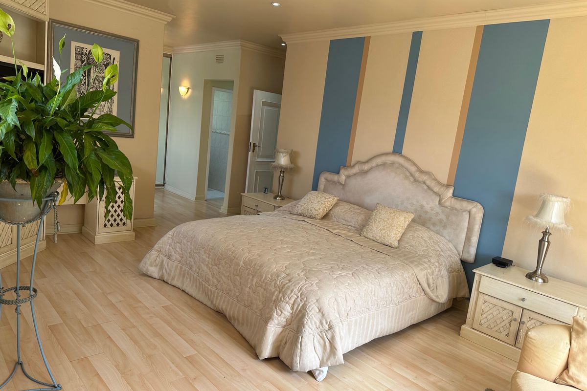 Spacious bedroom featuring light wood-look flooring, decorative wall paneling, and an integrated shelving unit, with an adjoining en-suite bathroom area.