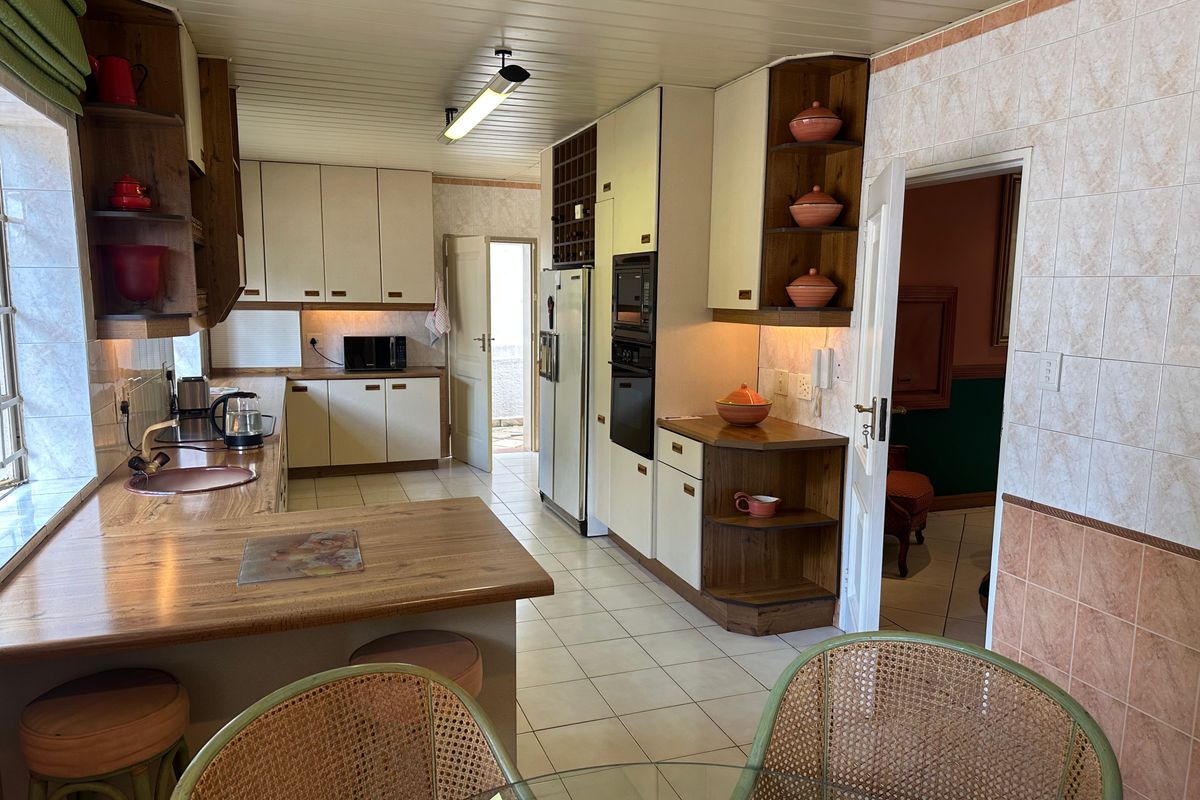 A functional kitchen featuring wood-look laminate countertops, built-in oven and microwave, ample cabinetry, and tiled flooring with direct access to an adjacent room.