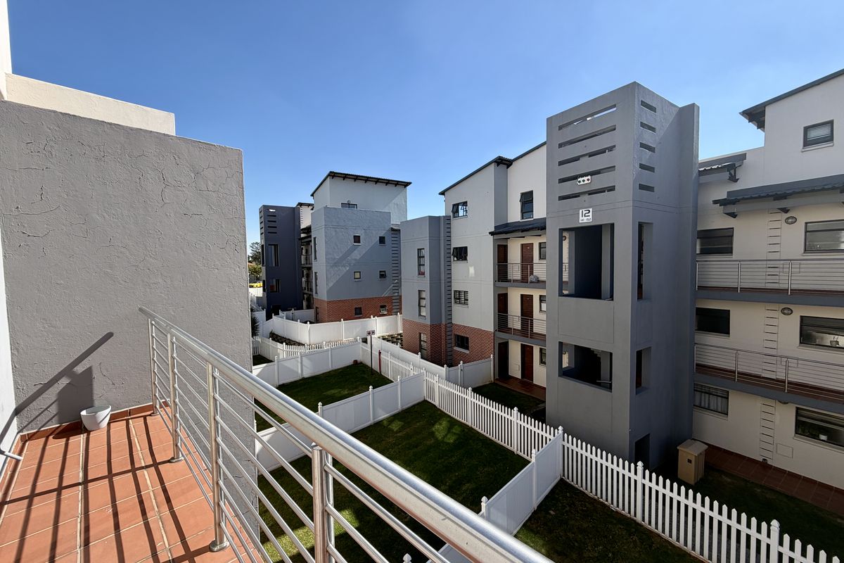 A view from an elevated balcony overlooking a shared garden area and the rear facade of a modern apartment complex.