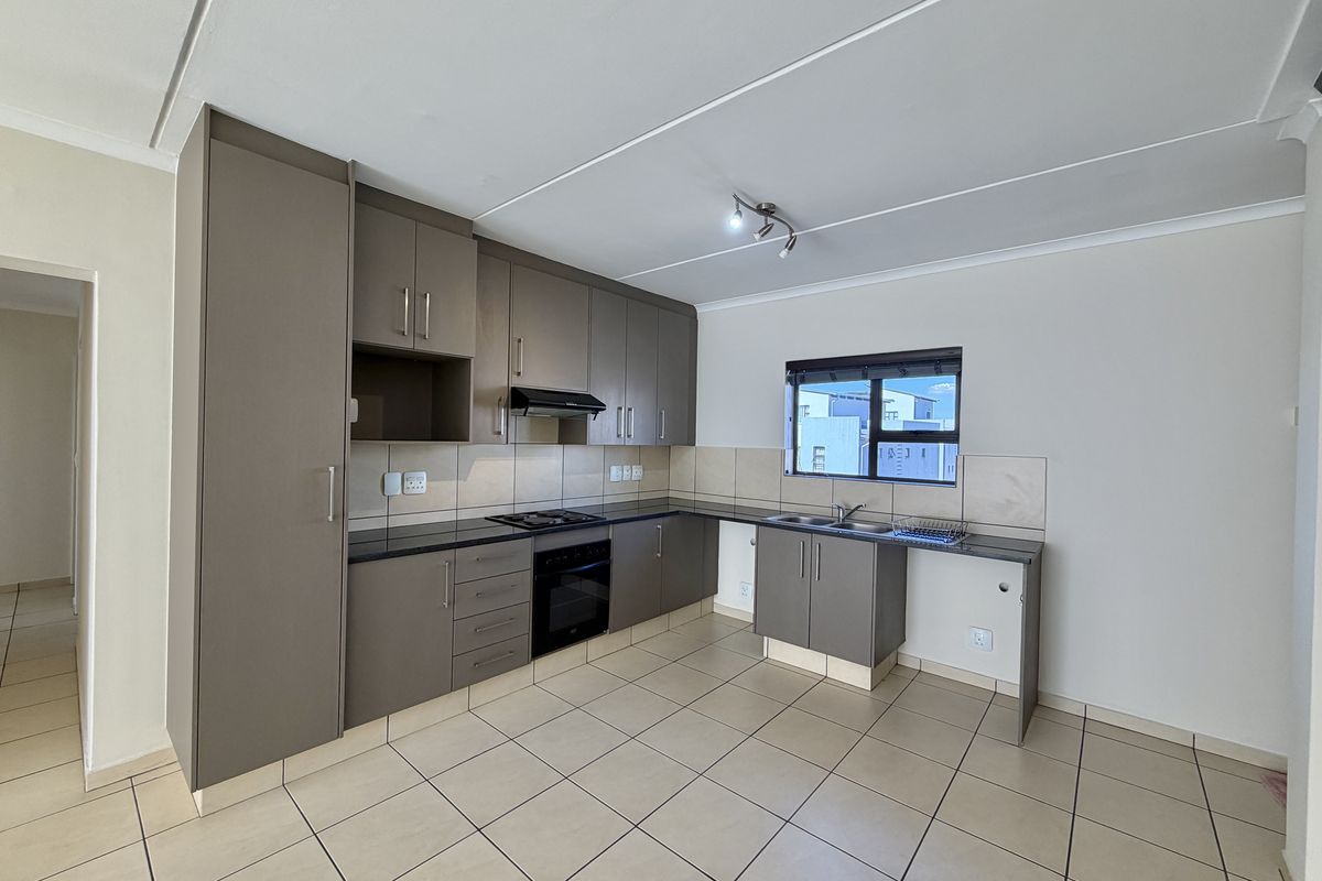 A clean, modern kitchen featuring neutral-toned built-in cabinetry, dark countertops, integrated oven and hob, and tiled flooring throughout.