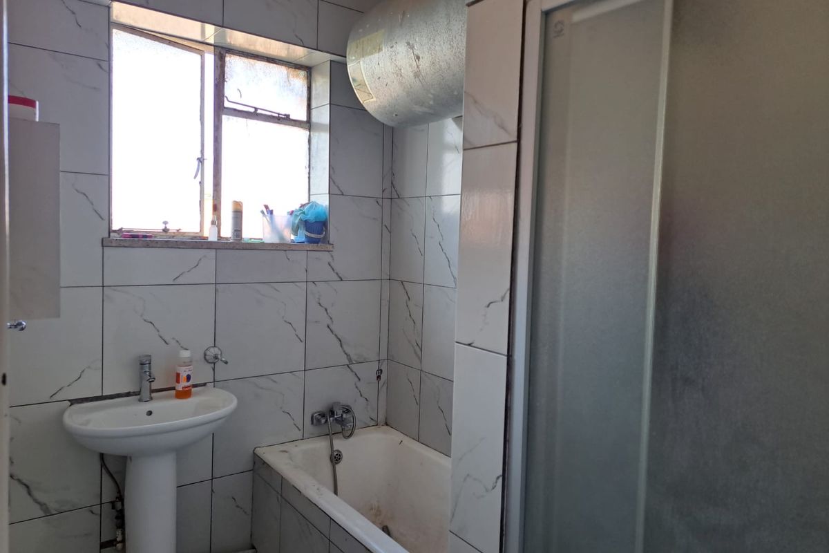 A functional bathroom featuring a pedestal basin, bathtub, and shower enclosure with tiled walls and an exposed geyser unit.