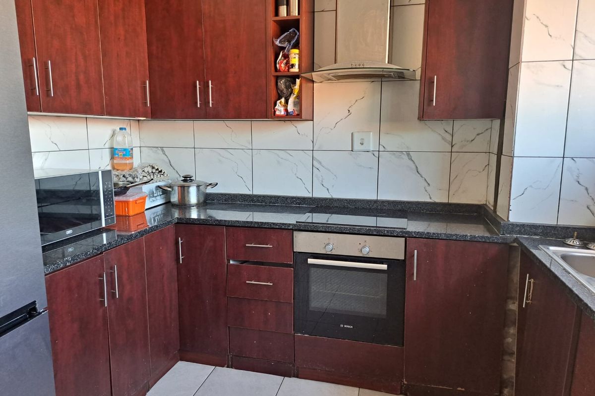 A functional kitchen featuring dark wood cabinetry, granite countertops, a built-in oven, electric hob, and a tiled backsplash.