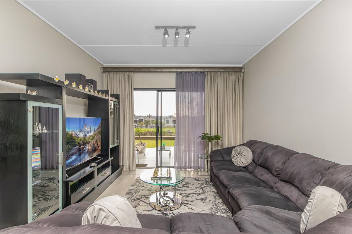 A comfortable living room featuring tiled flooring, a ceiling-mounted spotlight fixture, and large sliding glass doors that open onto a patio area.