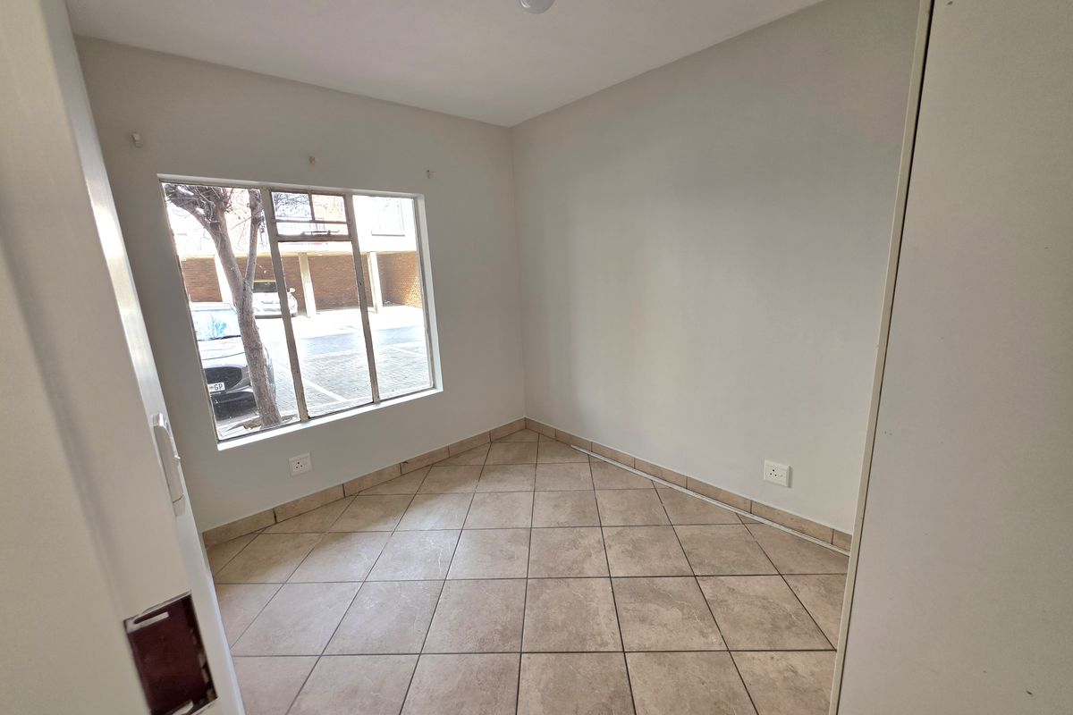 A vacant bedroom featuring neutral tiled flooring, large window with natural light, and built-in electrical outlets.