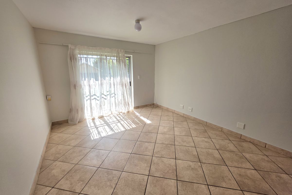 An empty living room featuring neutral tiled flooring and a sliding glass door providing access to the exterior.