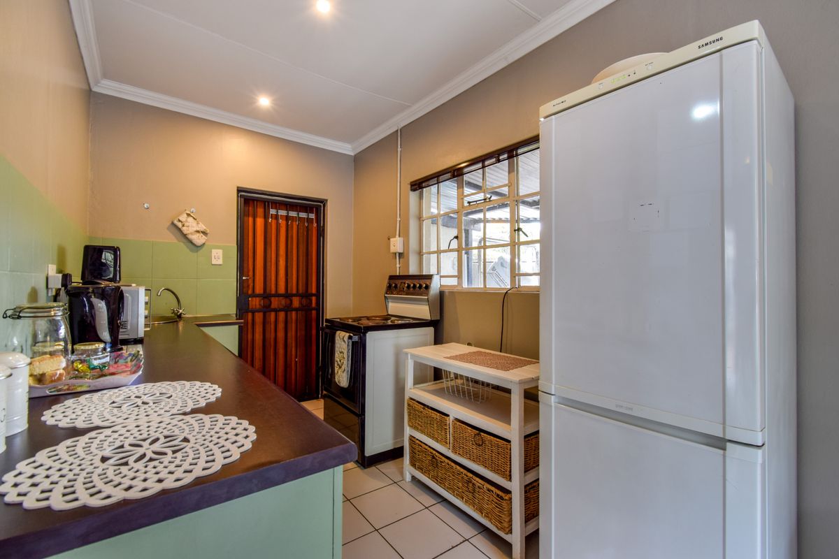 A functional kitchen featuring tiled flooring, laminate countertops, a built-in sink, and a security gate leading to the exterior.