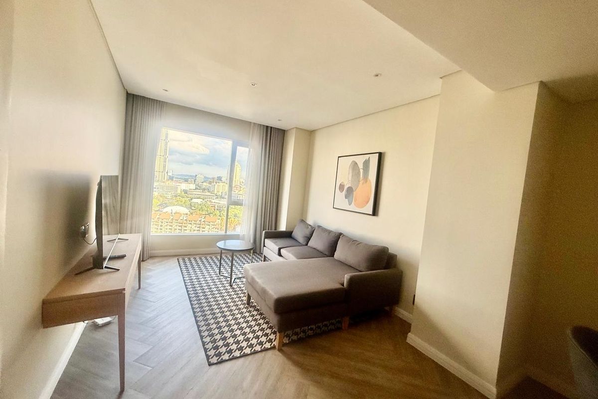 A bright and modern living room featuring herringbone timber flooring, recessed ceiling lighting, and a large window offering expansive city views.
