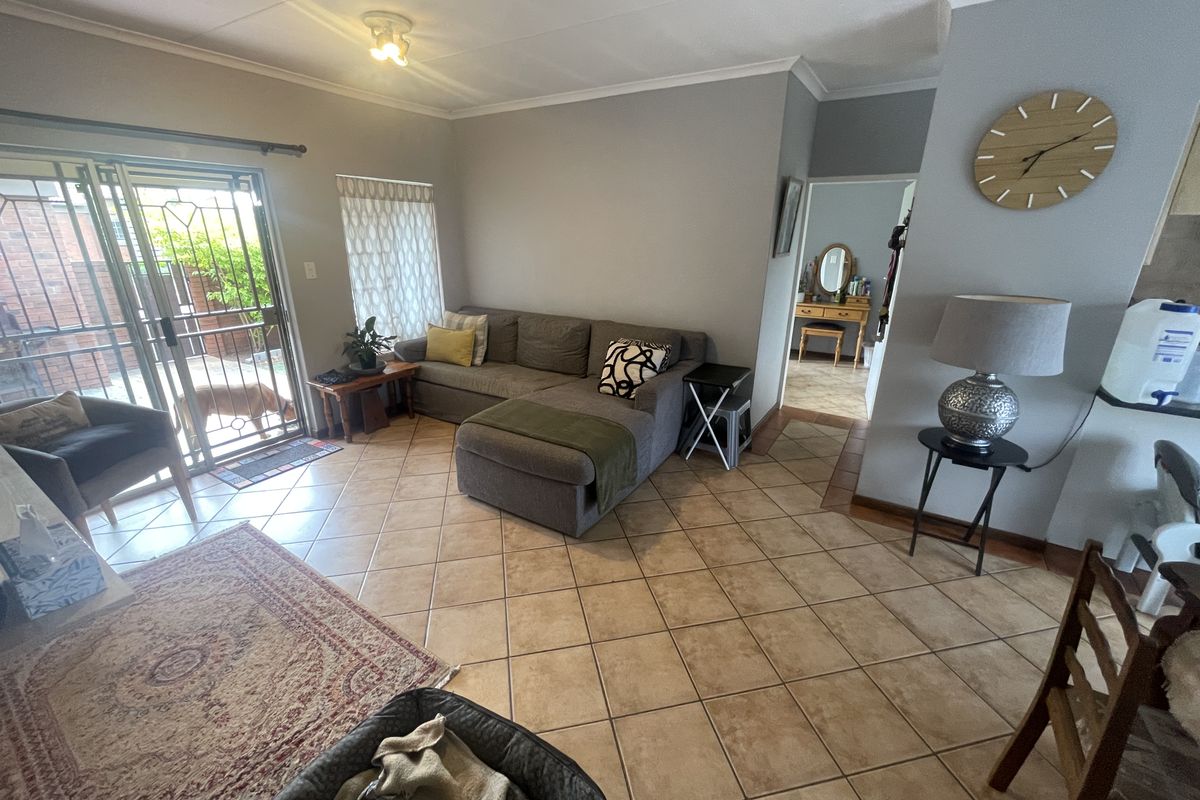 A living room featuring tiled flooring, a security gate leading to the exterior, and access to an adjacent room.