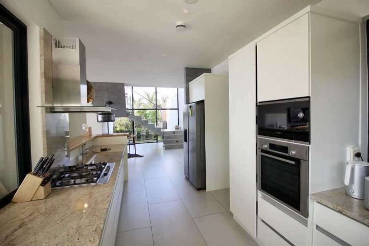 Modern kitchen featuring stone countertops, integrated stainless steel oven and microwave, gas hob, and sleek cabinetry, flowing into an open-plan living area.