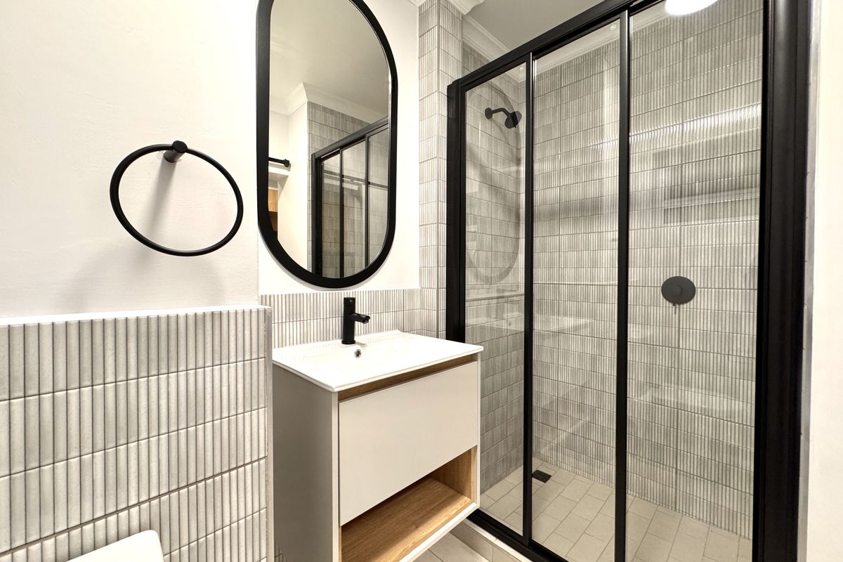 Modern bathroom featuring a floating vanity, black framed shower enclosure, vertical textured wall tiles, and a contemporary oval mirror.