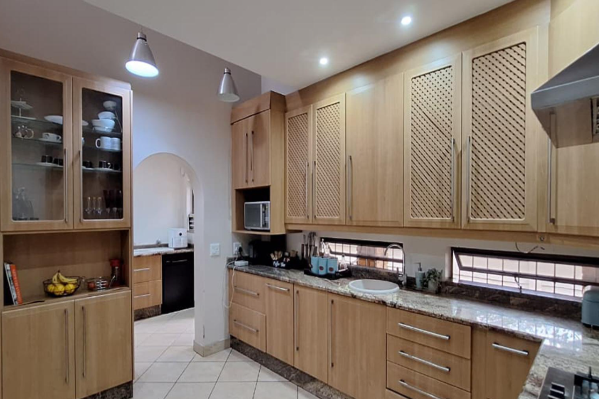 A well-appointed kitchen featuring light wood cabinetry, granite countertops, integrated storage, and a separate scullery area with tiled flooring.