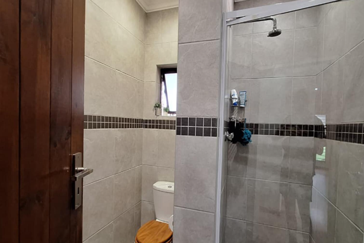 A modern bathroom featuring tiled walls with a decorative mosaic border, a glass-enclosed shower, and a toilet.
