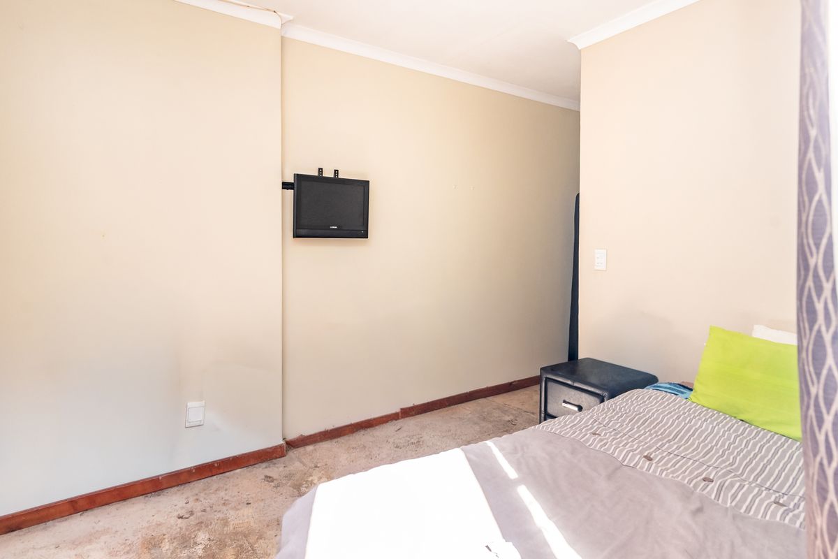 A bedroom featuring neutral walls, a wall-mounted television bracket, and worn carpeting, offering a blank canvas for potential renovation and flooring updates.