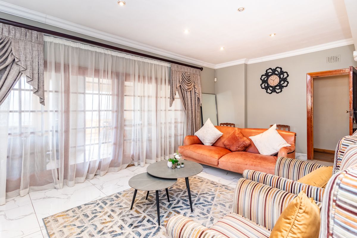 A bright living room featuring large glass sliding doors with elegant drapes, polished marble-style floor tiles, and recessed ceiling lighting.
