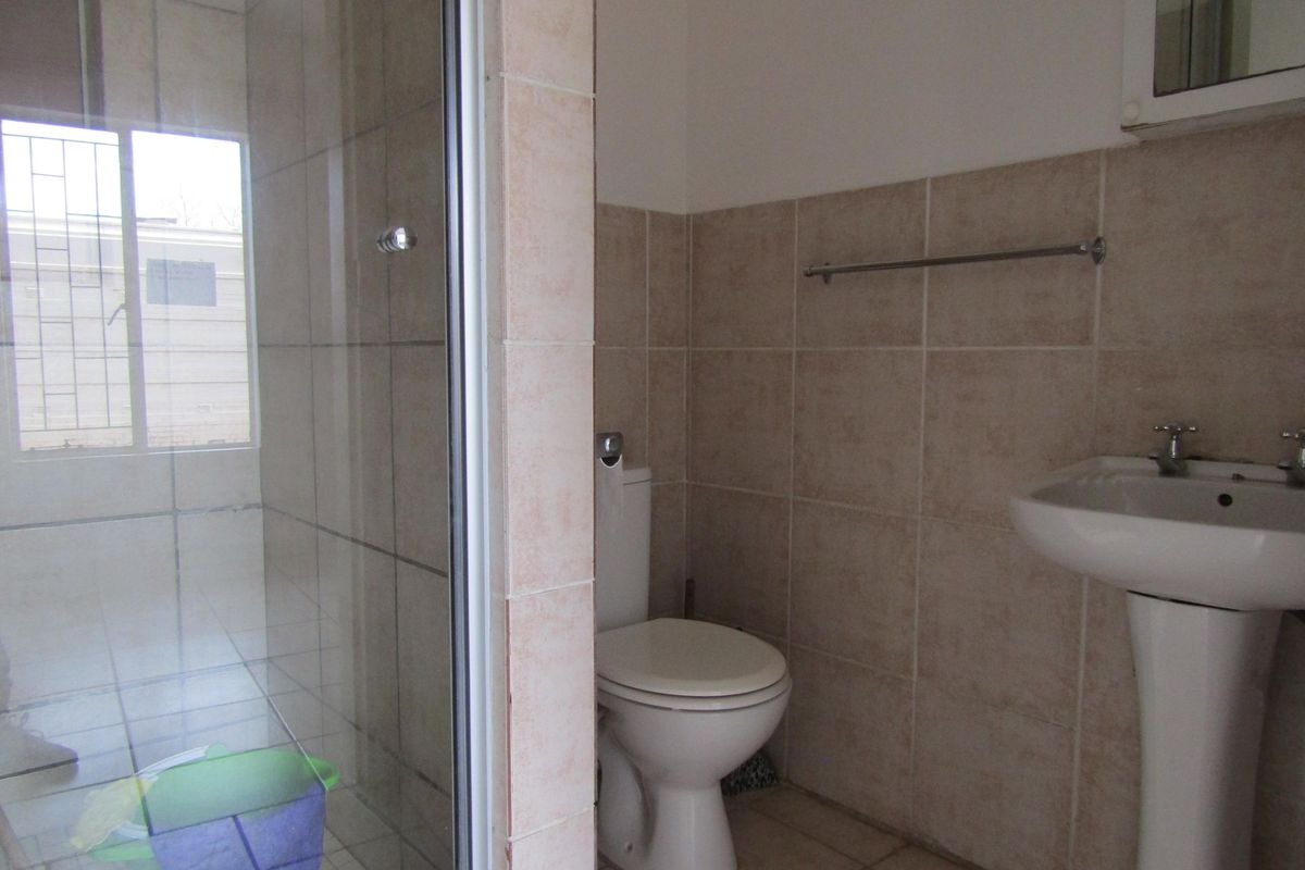 A functional bathroom featuring a glass-enclosed shower, pedestal basin, and toilet with neutral wall and floor tiling.