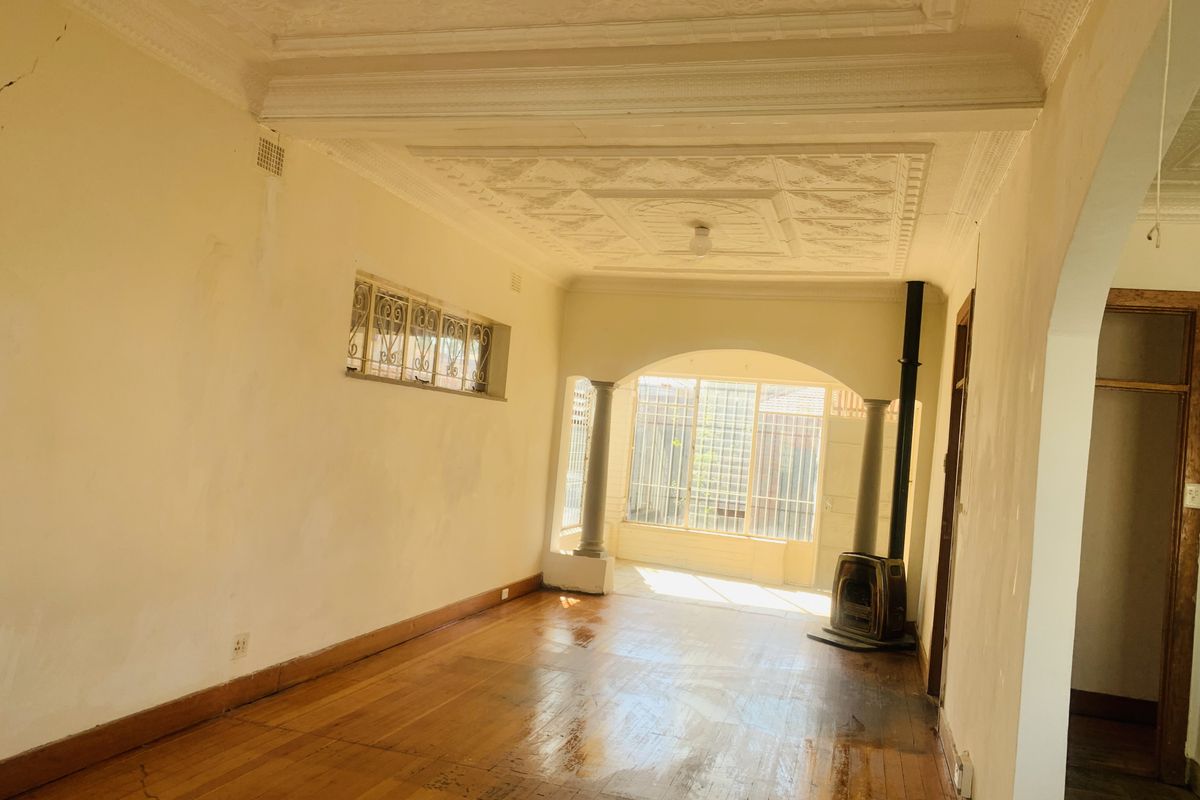 Spacious living area featuring original ornate ceiling details, polished timber flooring, and a built-in fireplace, leading to an enclosed sunroom area.