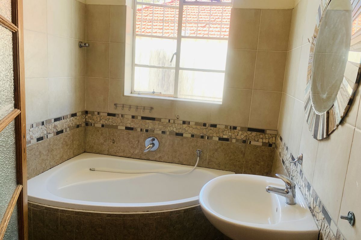 A functional bathroom featuring a corner bathtub, pedestal basin, and tiled walls with decorative mosaic accents.