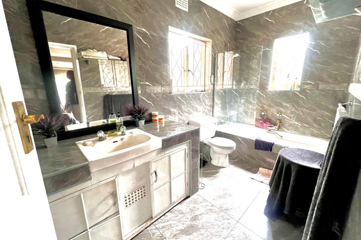 A full bathroom featuring floor-to-ceiling marble-look wall tiles, a built-in vanity with integrated basin, a bathtub with shower mixer, and a toilet.