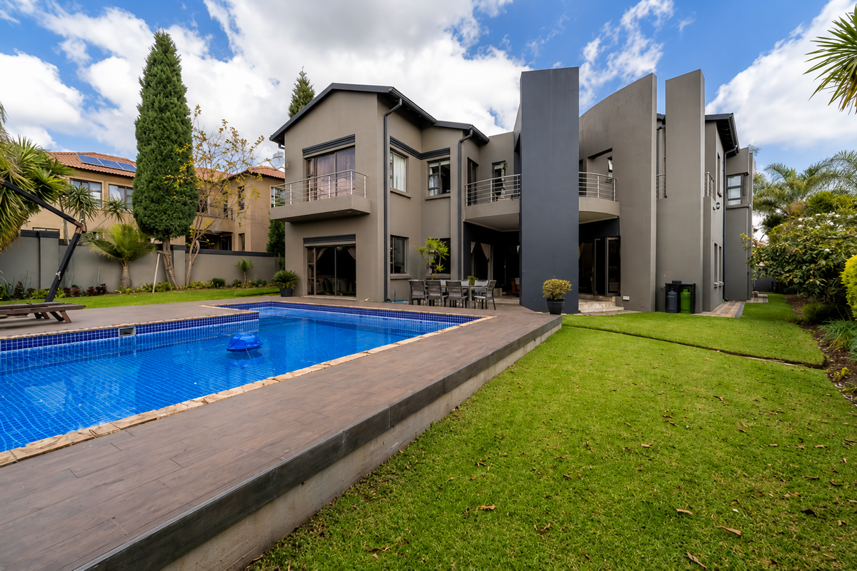 A modern rear exterior view featuring a swimming pool with tiled surround, landscaped lawn, and a multi-level dwelling with balconies.