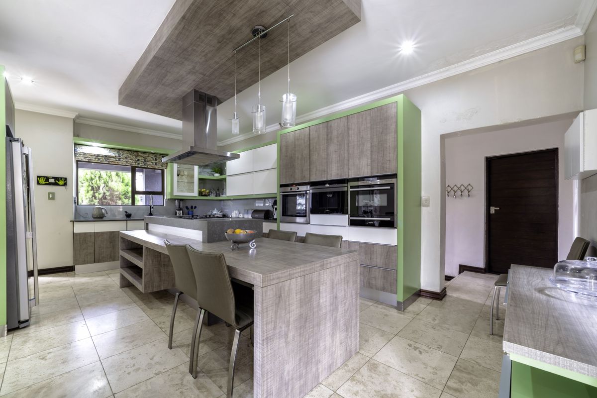 Modern kitchen featuring wood-grain cabinetry, green accents, a central island with integrated seating, and built-in stainless steel appliances.