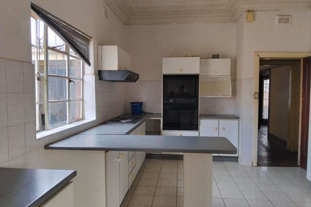 A dated kitchen featuring built-in cabinetry, a wall-mounted oven, a gas hob, and tiled flooring, offering a functional layout ready for modernization.