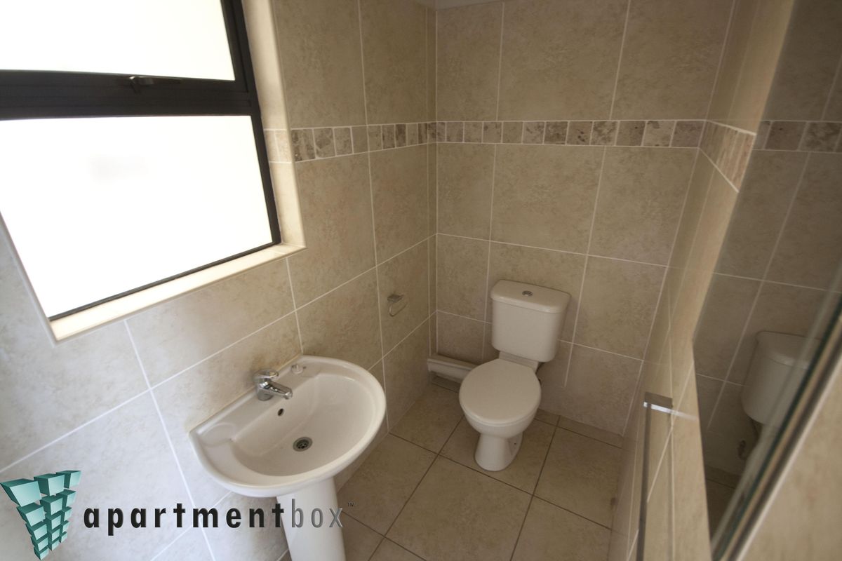 A compact bathroom featuring neutral wall and floor tiling, a pedestal basin, and a standard toilet.