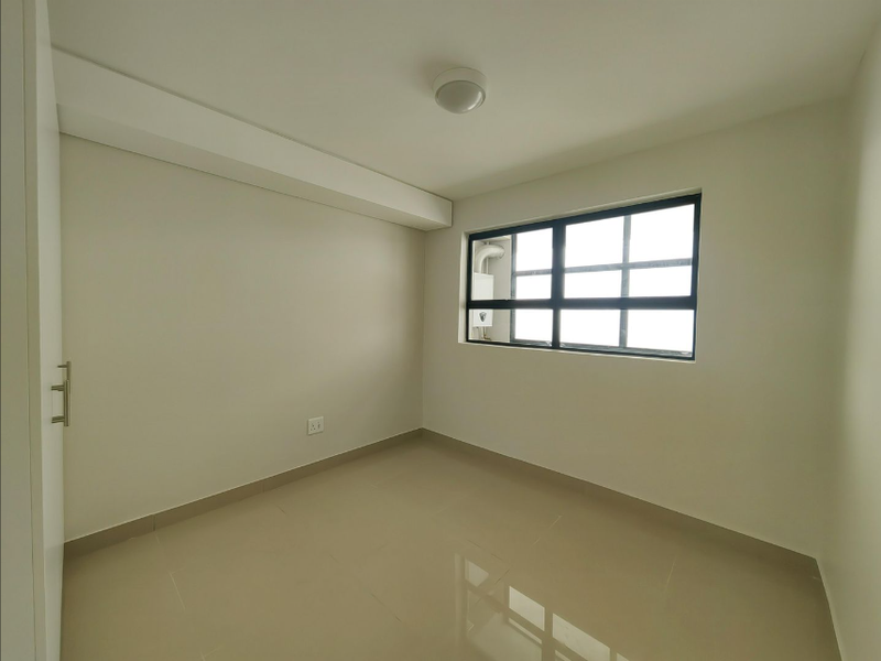 A clean, empty bedroom featuring neutral tiled flooring, a built-in cupboard, and a large window providing natural light.