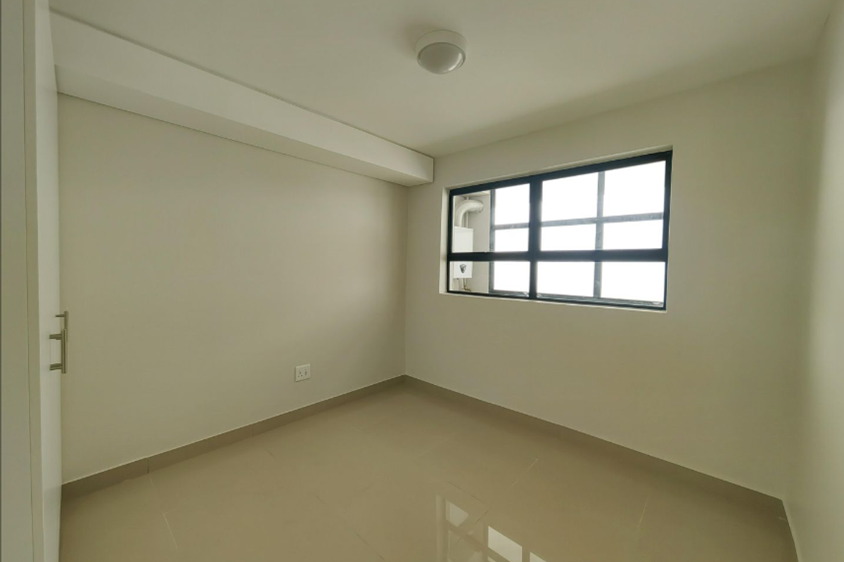 A clean, empty bedroom featuring neutral tiled flooring, a built-in cupboard, and a large window providing natural light.
