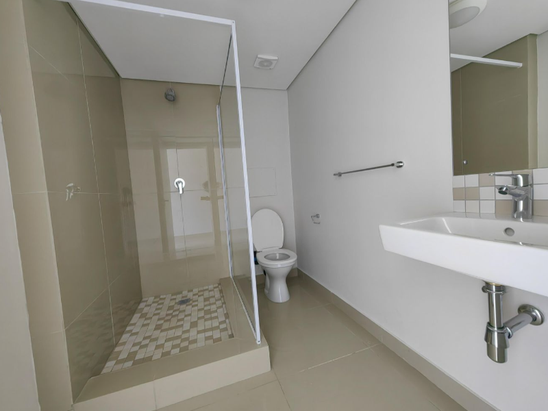 A clean, modern bathroom featuring a walk-in shower with glass screen, wall-mounted basin, and neutral floor-to-ceiling tiling.