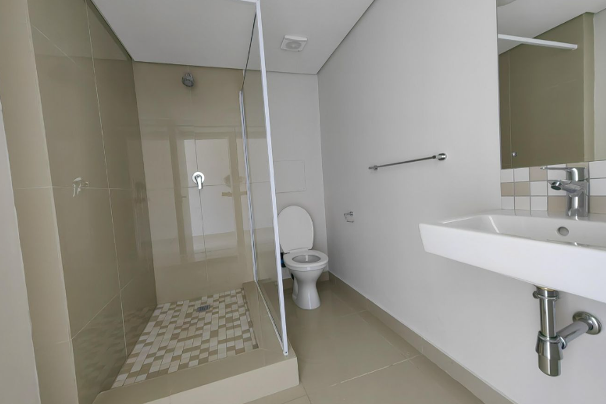 A clean, modern bathroom featuring a walk-in shower with glass screen, wall-mounted basin, and neutral floor-to-ceiling tiling.