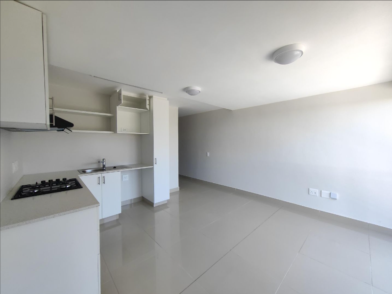 Modern open-plan living area featuring a compact kitchen with built-in cabinetry, gas hob, and sleek tiled flooring throughout.
