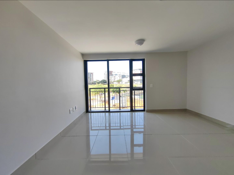 A bright, empty living area featuring large sliding glass doors that open to a balcony, finished with neutral floor tiles.