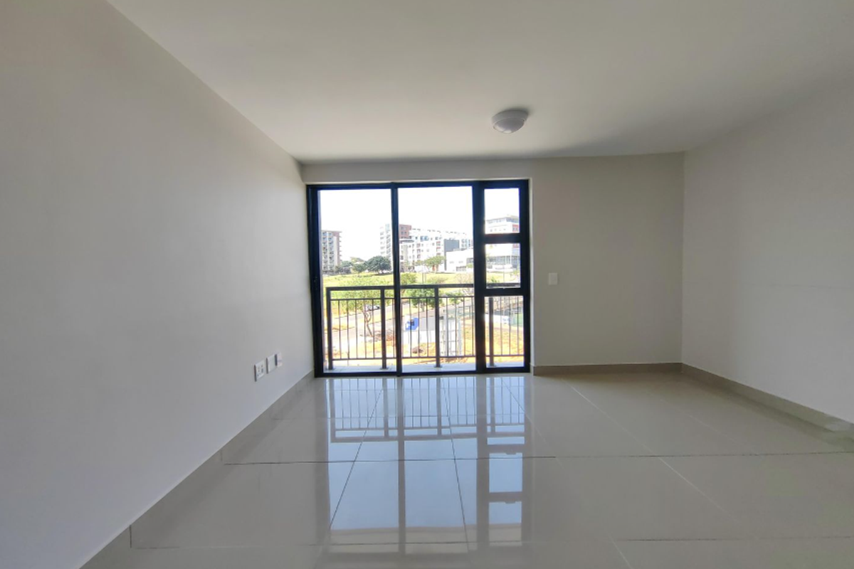 A bright, empty living area featuring large sliding glass doors that open to a balcony, finished with neutral floor tiles.
