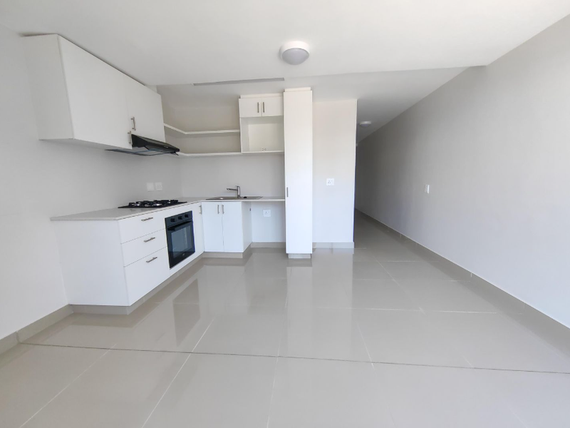 A clean, modern kitchen featuring white cabinetry, a gas hob, built-in oven, and tiled flooring in an open-plan layout.