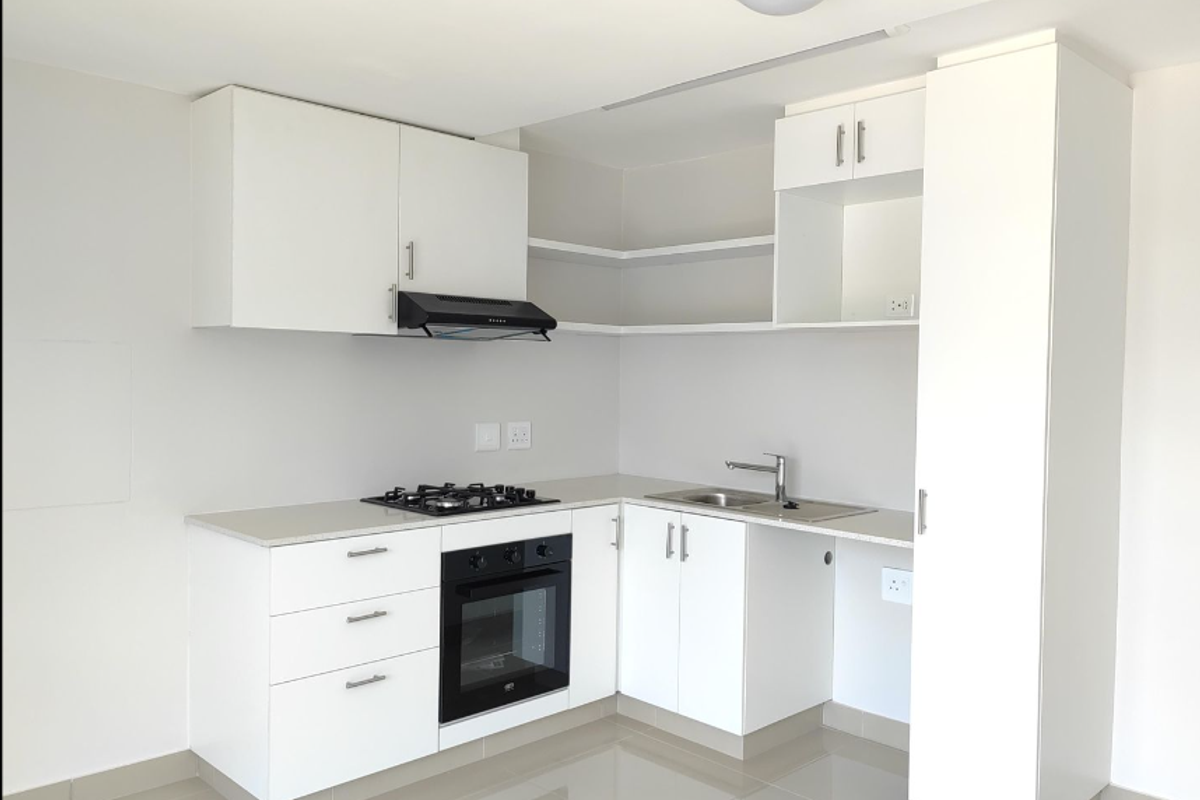 Modern, clean-lined kitchen featuring white cabinetry, stone countertops, integrated gas hob, oven, and extractor fan, with neutral tiled flooring.